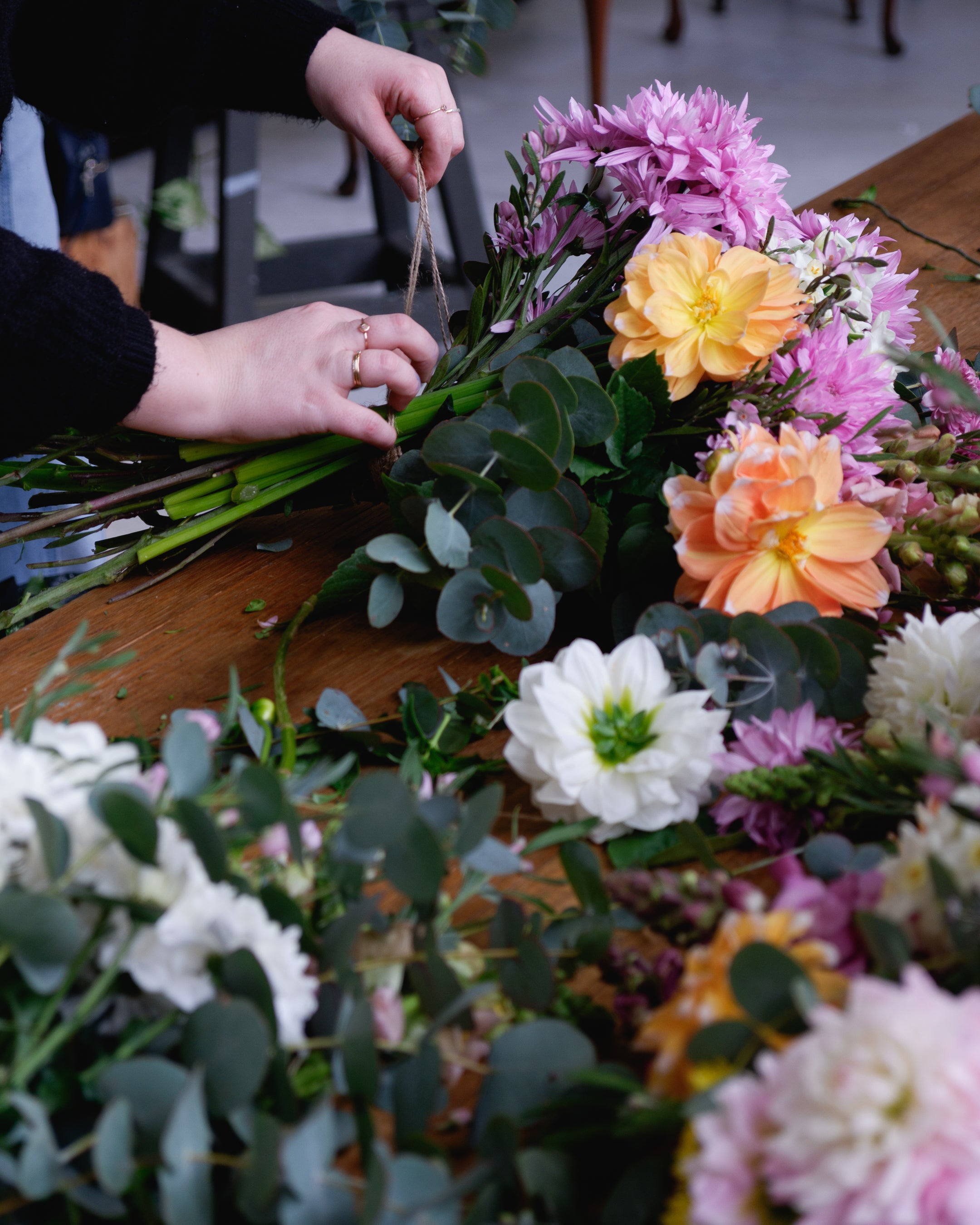 Workshop table with flowers, foliage as student ties bunch with string.