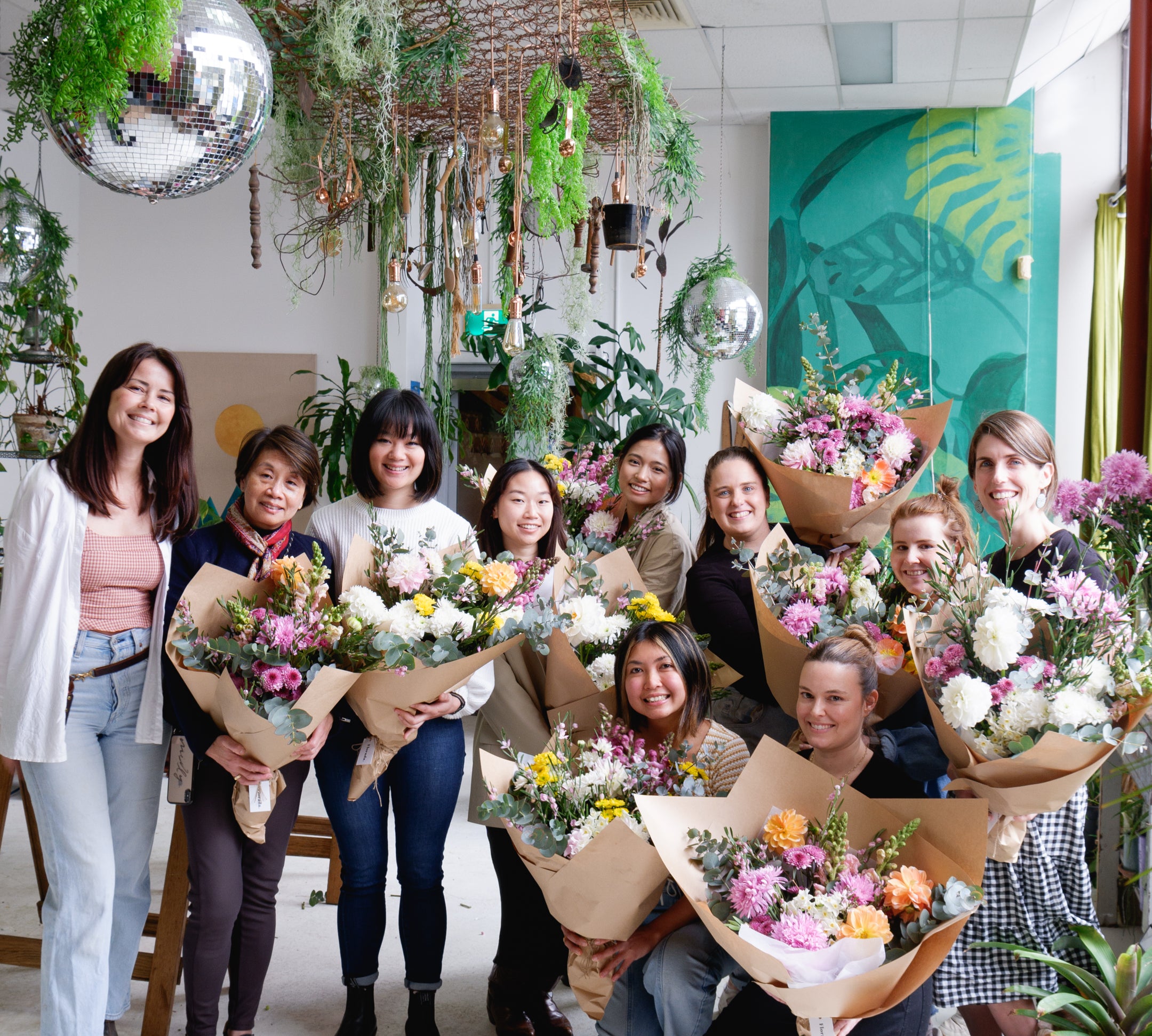 Group shot of flower workshop attendees holding finished, wrapped bunches with florist.