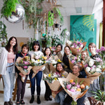 Group shot of flower workshop attendees holding finished, wrapped bunches with florist. 