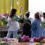 Group shot of flower workshop class, students selecting flowers with florist to create their arrangement.