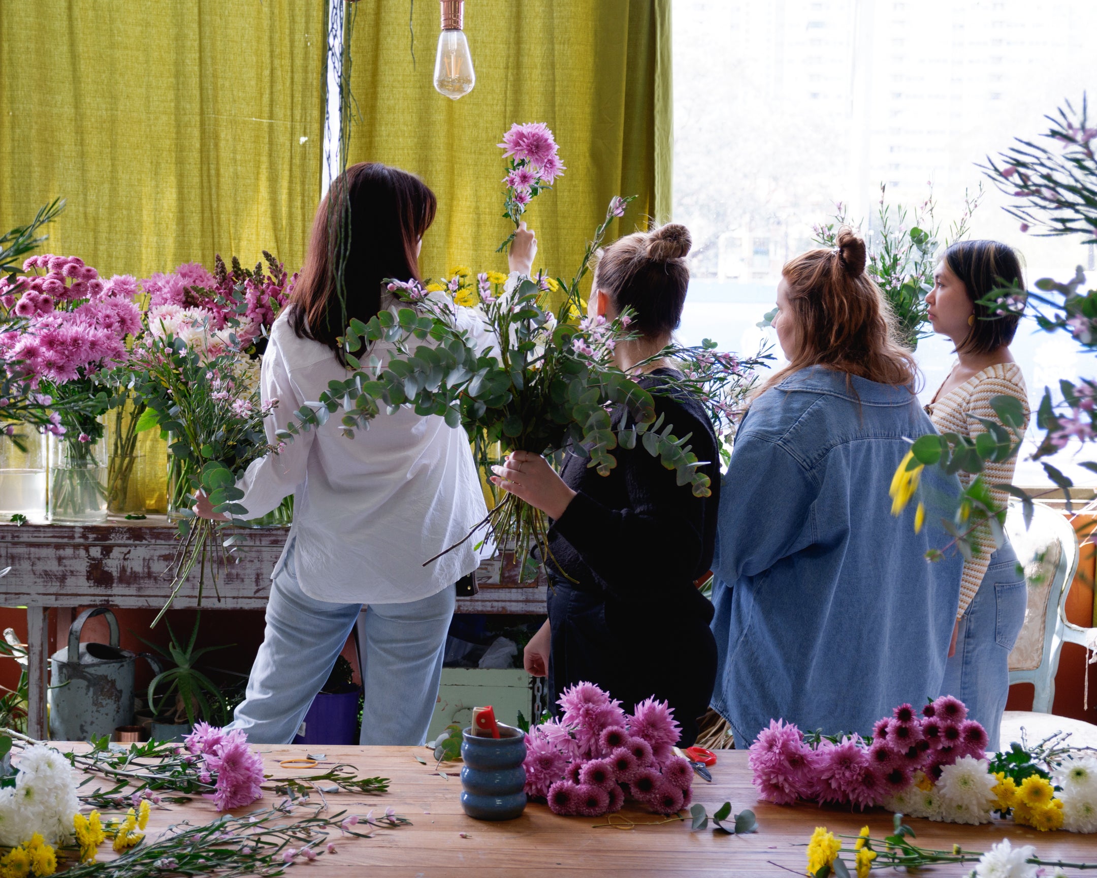 Group shot of flower workshop class, students selecting flowers with florist to create their arrangement.