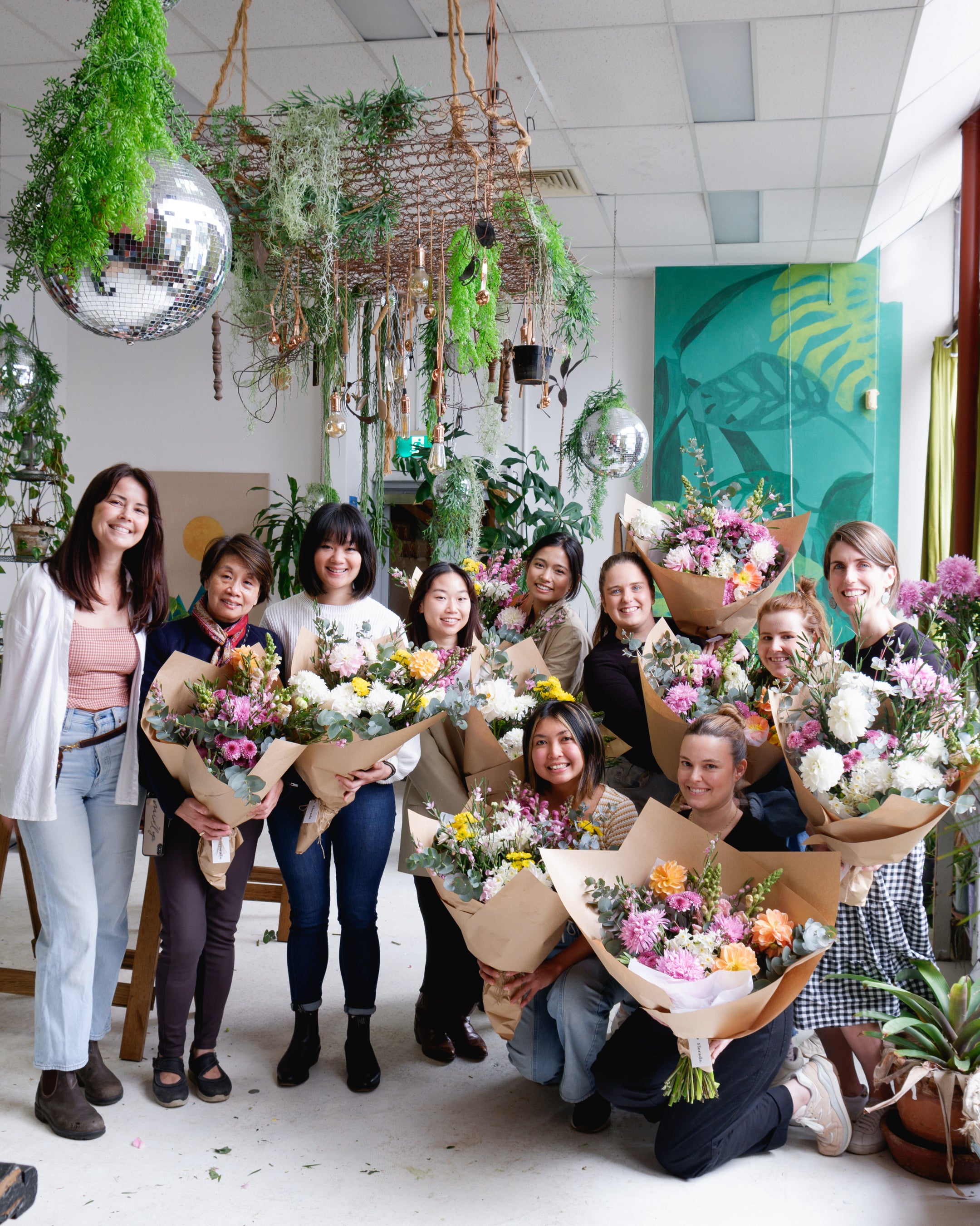 Group shot of flower workshop attendees holding finished, wrapped bunches with florist.
